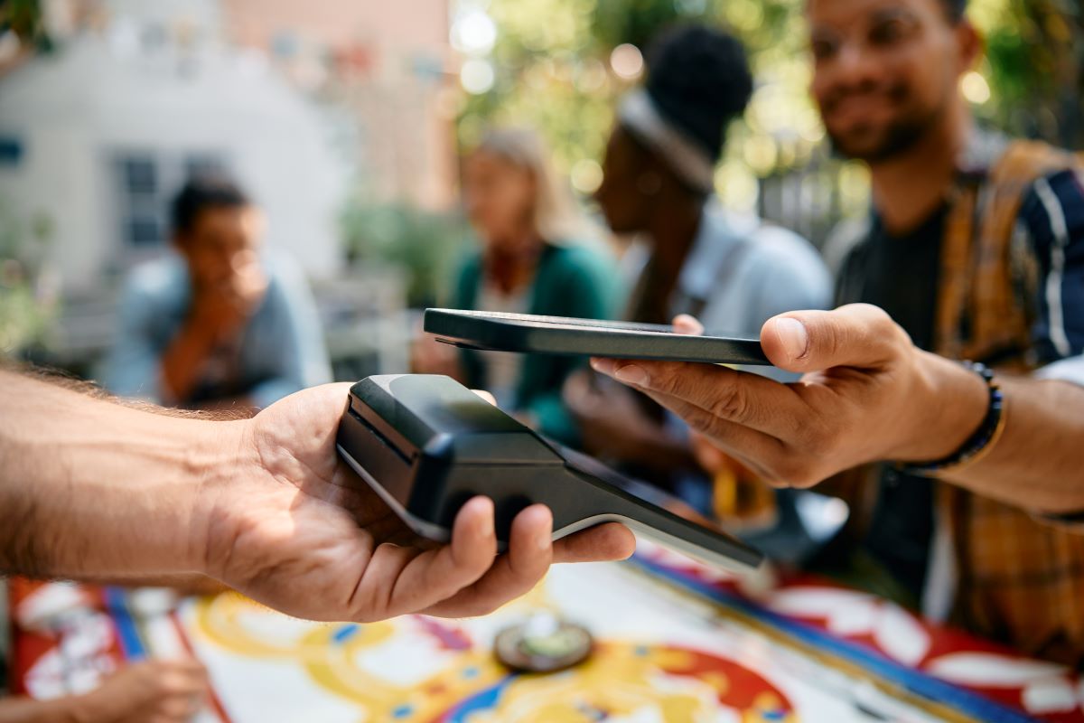 Imagem aproximada de um homem usando um smartphone enquanto paga a um garçom em um café