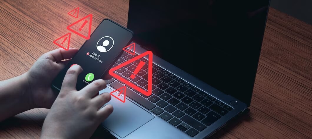 Pessoa recebendo ligação suspeita no celular enquanto senta de frente para computador