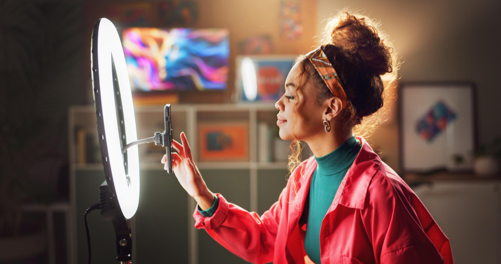 Mulher se prepara para gravar com celular em frente a ring light, em ambiente moderno e colorido.