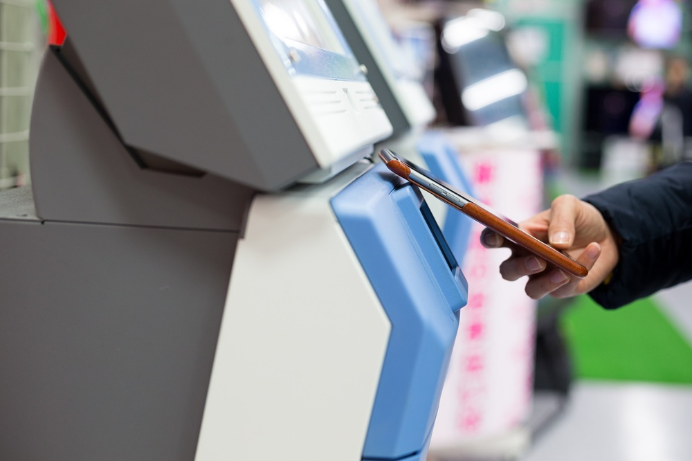 Pessoa utilizando o celular para pagamento em terminal de self-checkout.
